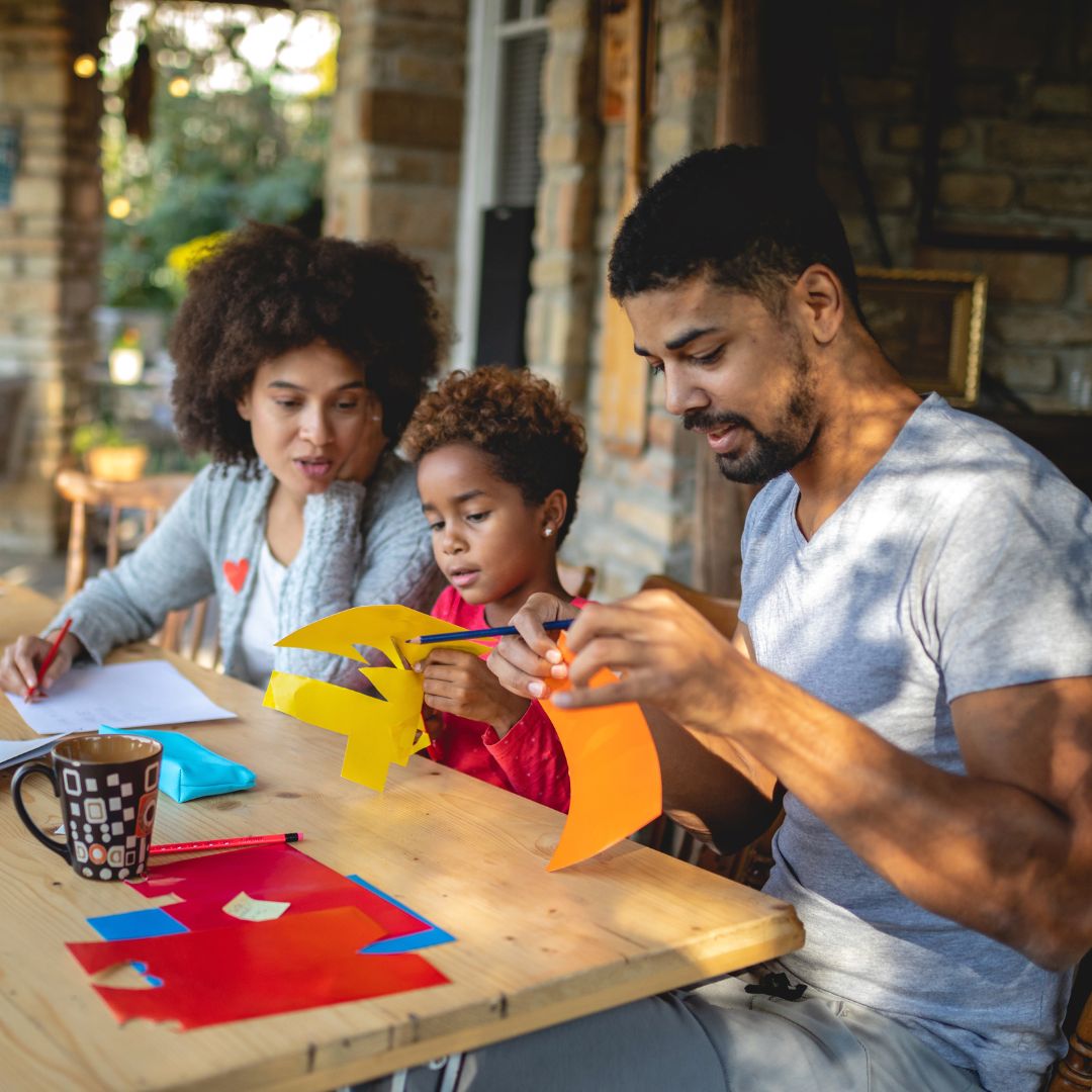 a family sitting at a table doing a paper craft