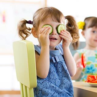 Little Girl Holding Cucumbers Over Her Eyes